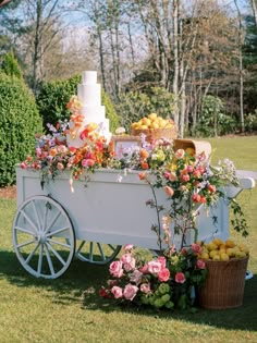 a white cart filled with lots of flowers and fruit on top of a grass covered field