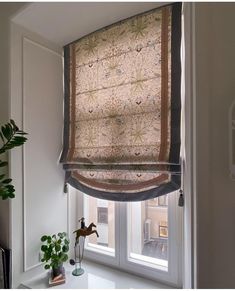 a window with a roman blind in the corner and a potted plant next to it