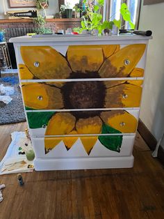 a painted dresser with sunflowers on the front and bottom drawers, sitting in a living room