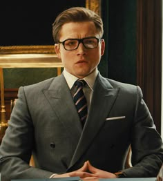 a man in a suit and tie sitting at a desk with his hands folded out