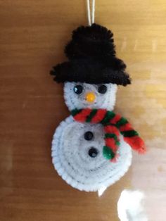 a crocheted snowman ornament hanging from a string on a table