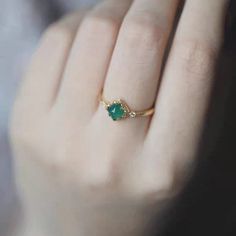 a woman's hand with a gold ring and green stone on top of it