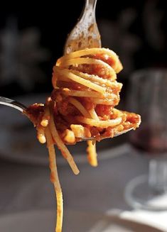 a fork full of spaghetti with sauce and cheese on it, ready to be eaten