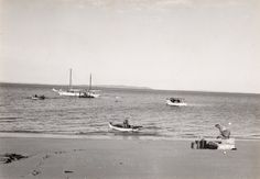 an old black and white photo of people on the beach with boats in the water