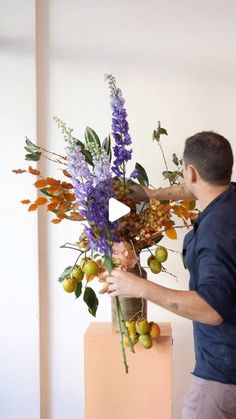 a man arranging flowers in a vase on top of a wooden box with leaves and berries