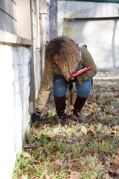 a woman bending down to pick up leaves from the ground outside her house with a shovel