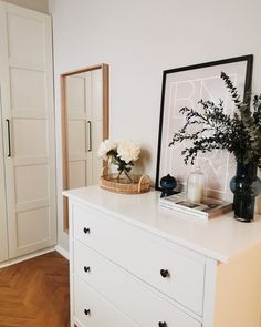 a white dresser topped with lots of drawers next to a vase filled with flowers and candles