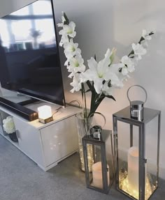 two vases with flowers and candles are next to a flat screen tv