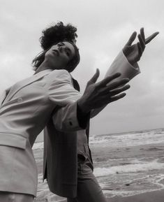 a man and woman standing next to each other near the ocean with their hands in the air