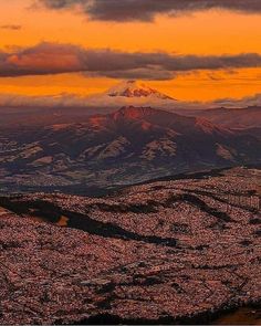 the sun is setting over a city with mountains in the background and clouds above it