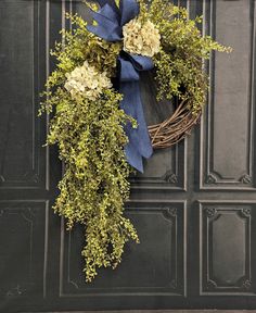 a wreath with blue ribbon hanging on the side of a building, decorated with flowers and greenery