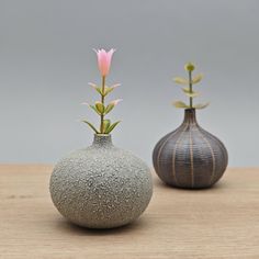 two vases with flowers in them sitting on a wooden table next to each other