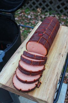 sliced meat sitting on top of a wooden cutting board next to a bbq grill