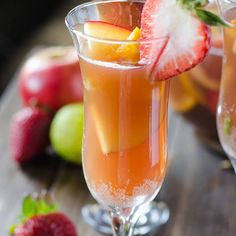 two glasses filled with liquid and fruit on top of a wooden table next to some strawberries