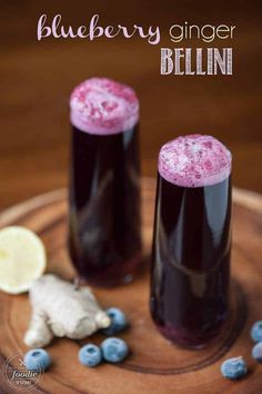 two glasses filled with blueberry ginger bellin sitting on a plate next to lemons