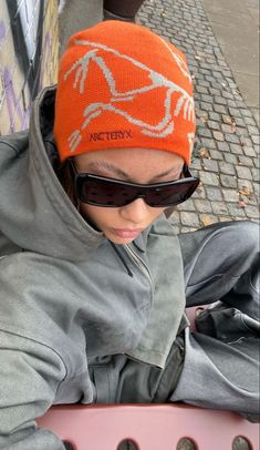 a young boy wearing sunglasses and an orange hat is looking down at his cell phone