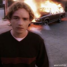 a young man standing in front of a burning car