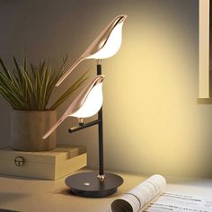 a desk lamp sitting on top of a table next to an open book and plant