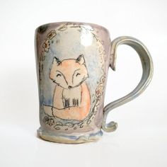 a ceramic mug with a fox painted on the front and sides, sitting on a white surface