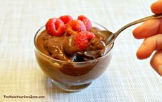 a person is holding a spoon over a bowl of chocolate pudding with raspberries