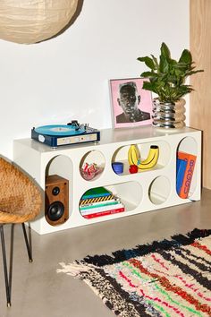 a white shelf with various items on it and a plant in the corner next to it