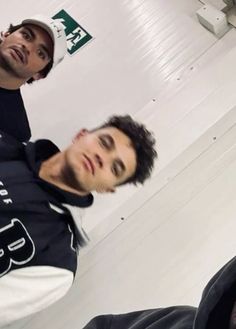 two young men sitting next to each other in a room with white walls and flooring