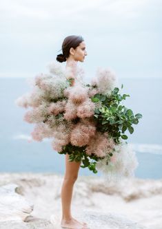 a woman standing on top of a cliff holding a bouquet of pink and white flowers