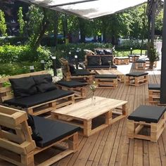 an outdoor seating area with black cushions and wooden furniture on a deck surrounded by greenery