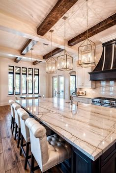 a large kitchen with marble counter tops and wooden beams on the ceiling is lit by pendant lights