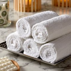 several white towels stacked on top of each other in front of a plate with soaps