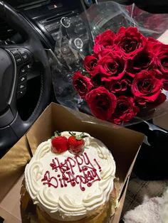 a birthday cake in a box with roses on the table next to it and a car steering wheel