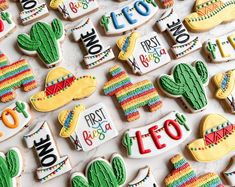 many decorated cookies are arranged on a table with the words first fiesta written in different languages