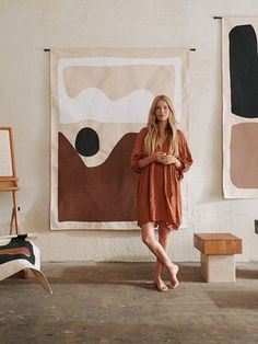 a woman standing in front of two paintings on the wall with her arms crossed and legs crossed