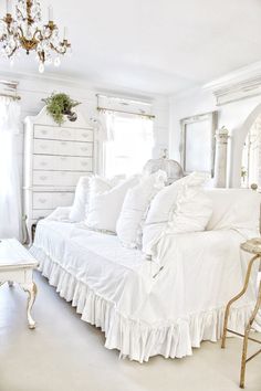 a white couch with ruffles and pillows on it in front of a chandelier