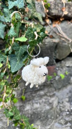 a white sheep keychain hanging from a tree with ivy growing on it's sides