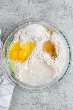 two eggs and flour in a glass bowl on a gray counter top next to a white towel