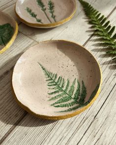 three bowls with green leaves painted on them sitting on a table next to a plant