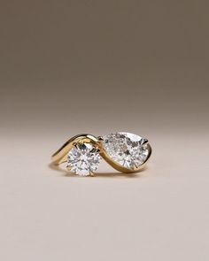 two pear shaped diamond engagement rings in yellow gold with diamonds on each side, set against a neutral background