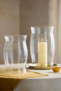 two clear glass vases sitting on top of a table next to a lit candle