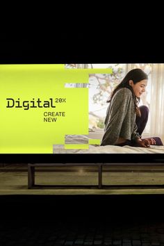 a woman sitting on a bench in front of a large screen with the words digital next to her