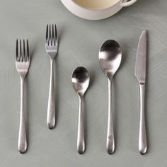 five forks, two spoons and one knife on a table with a cup of milk