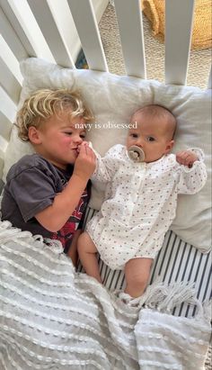 two young children laying in a crib and one is holding a pacifier to his mouth