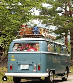 an old vw bus with luggage on top driving down the road in front of some trees