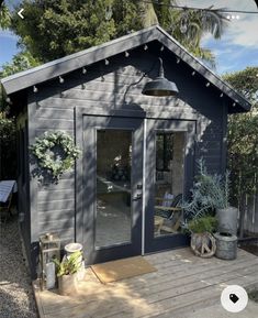 a small gray shed sitting on top of a wooden deck with potted plants next to it