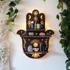 a wall mounted shelf with candles and rocks on it next to a potted plant