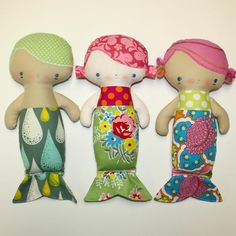 three little dolls are standing next to each other on a white surface, one is wearing a colorful dress and the other has a pink headband