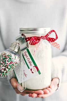 a person holding a mason jar filled with candy canes and other holiday decorations in their hands