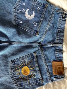 the back pocket of a pair of blue jeans with embroidered sun and moon on them