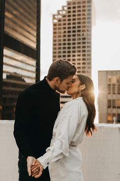 a man and woman standing next to each other in front of tall buildings with the sun shining down on them