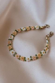 a beaded bracelet with pearls and green beads on a white cloth background is shown